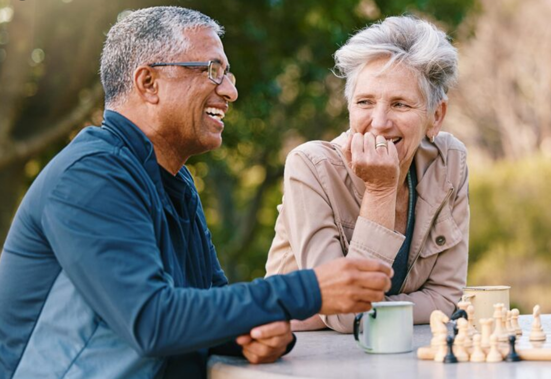 Mature couple laughing while playing chess outdoors